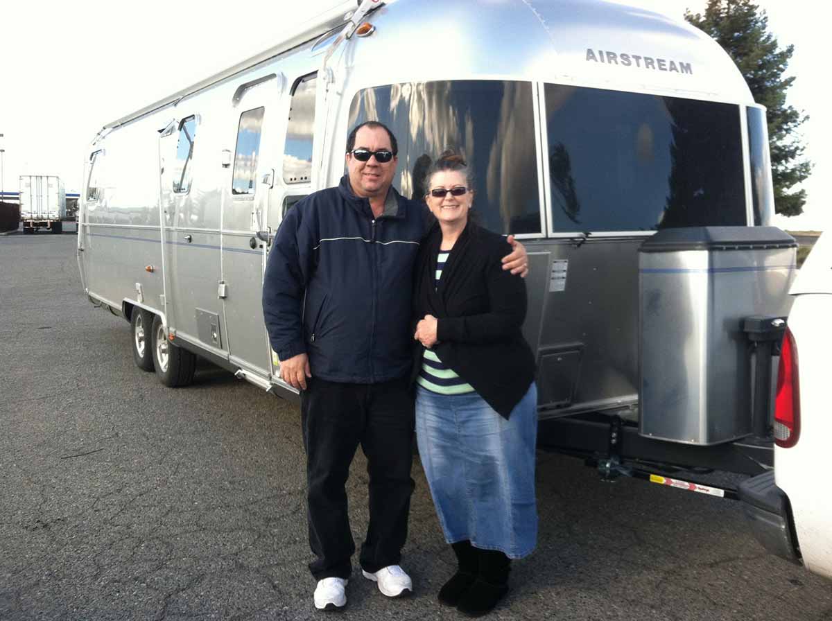 Man And Wife Standing Outside Silver Airstream Camper.