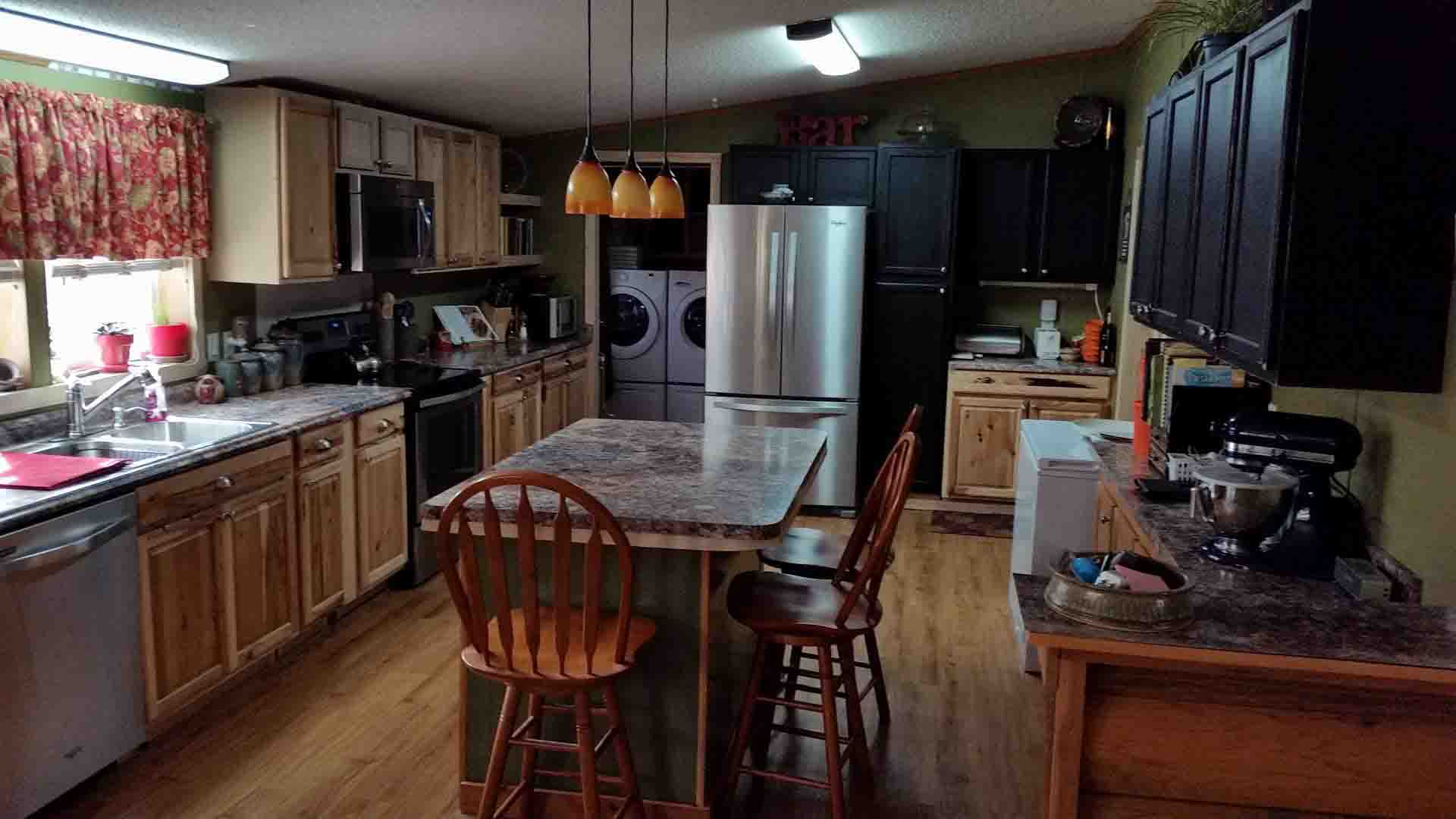 Kitchen With Stone Counter Tops And Black Cabinets On One Side And Wood Cabinets On The Other.