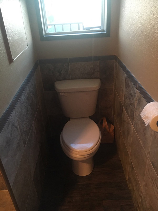 Small Bathroom With The Bottom Half Of The Wall In Stone Tile And Dark Wood Flooring.
