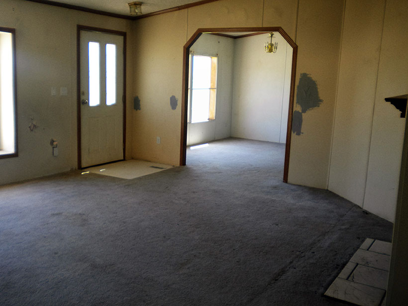 Living And Dining Room With Stained White Carpet, Yellow Patched Walls With Holes In Them.