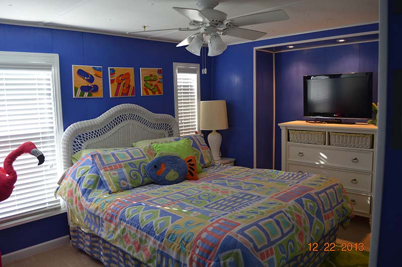 Bright Blue Walled Bedroom With White Accent Pieces And A Recessed Area Housing A Dresser And TV.