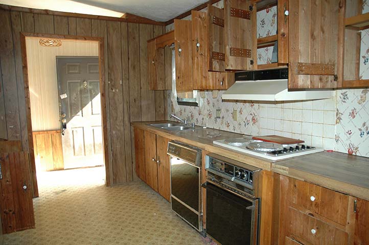 Kitchen With very Old Appliances, Vinyl Flooring, And Wood Paneling And Cabinets.