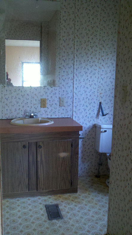 Bathroom With Floral Wallpaper, Vinyl Flooring And An Aged Sink And Cabinet.