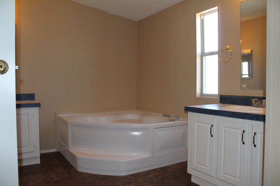 Bathroom With A Large Corner Tub Tan Walls, And White Cabinets.