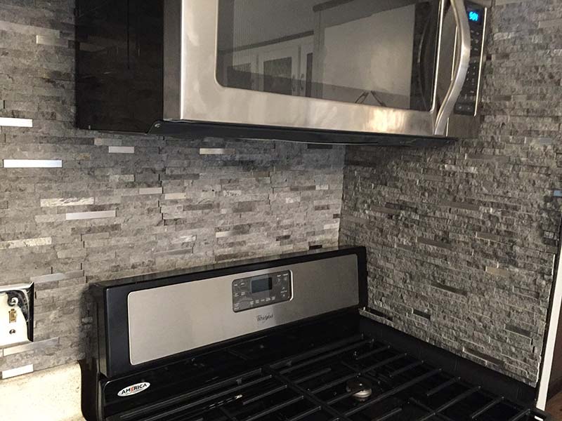 Black And Stainless Steel Stove, With Stone Backdrop On The Wall.