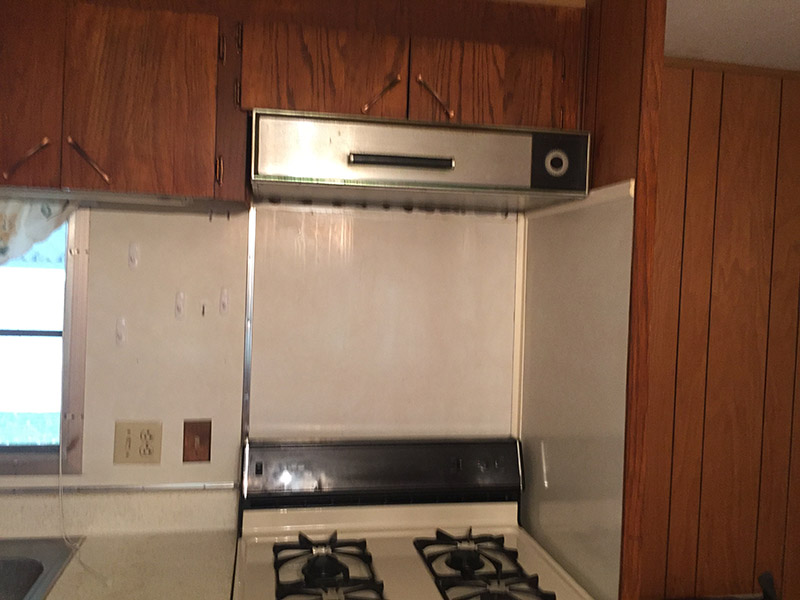 Older Kitchen Stove With An Outdated Overhead Fan and Old Wooden Cabinets.