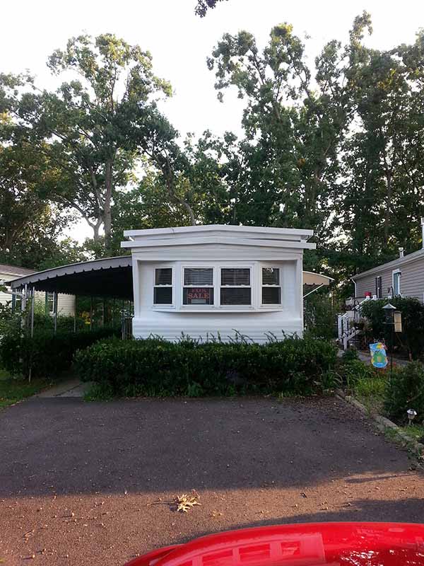 Outside Of A Mobile Home With Four Windows Across The Front And An Awning Over The Door.