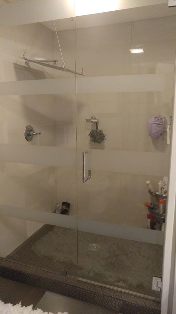 White tiled Shower With Full Glass Doors With Bands Of White Horizontally Across.