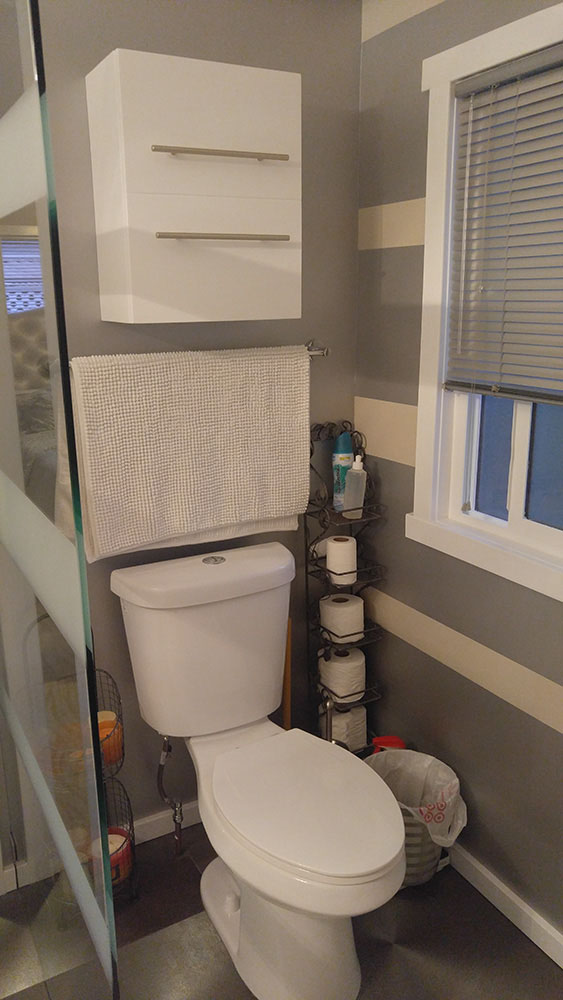 Another View Of the Bathroom, Showing The White Toilet And Cabinet, And Grey And White Banded Walls.