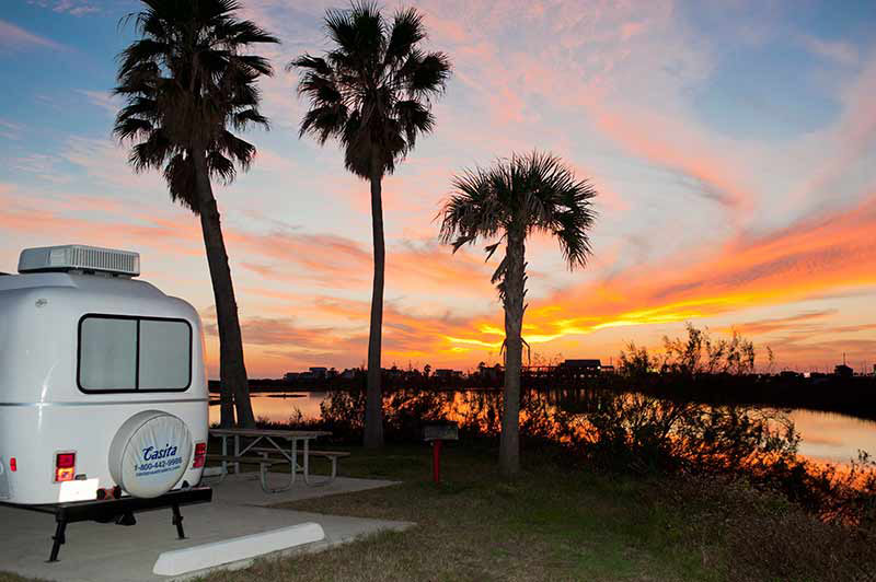Camper Parked By Palm Trees And A Lake.