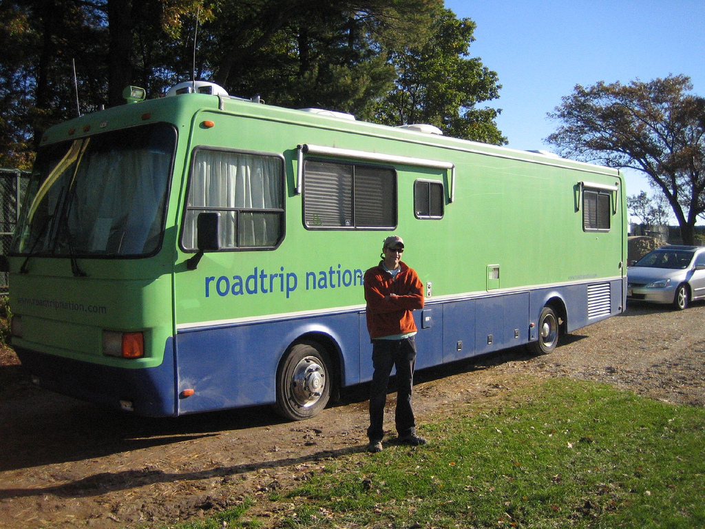 Man Standing Outside Green And Blue Road Trip Nation RV.