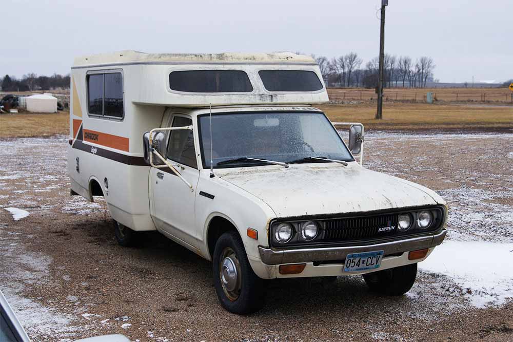 White Datsun Camper Truck Parked In A Snowy Parking Lot.