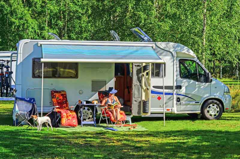RV With A Woman Reading Under The Awning.